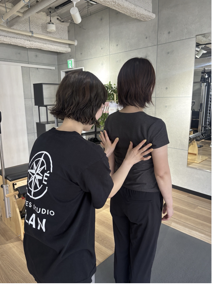 立った姿勢を確認しながらピラティス指導を行うトレーナー